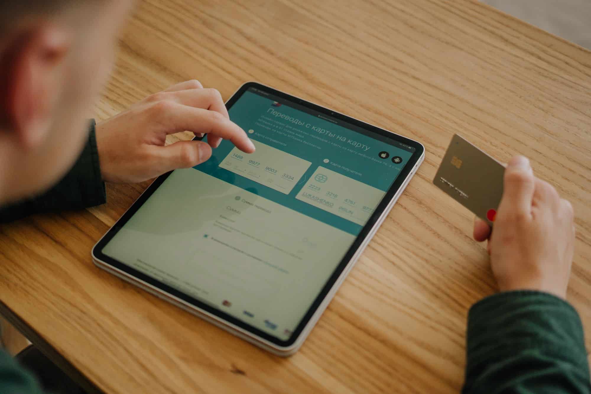 Ahşap masada tablet üzerinde ödeme bilgilerini giren ve banka kartı tutan kişi