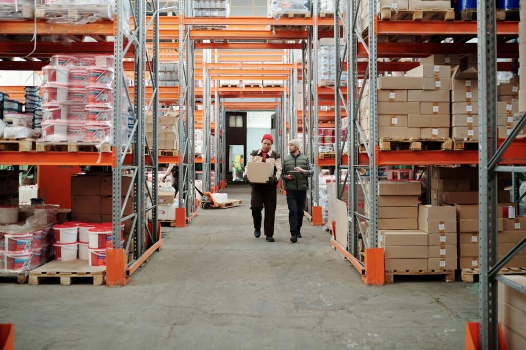 Depo rafları arasında yürüyen iki çalışan, e-ticaret operasyonu ve stok süreci